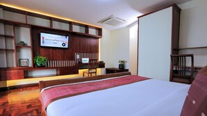 Una camera d'albergo con un letto grande, una testiera in legno, una TV a schermo piatto fissata al muro e un pavimento in legno.