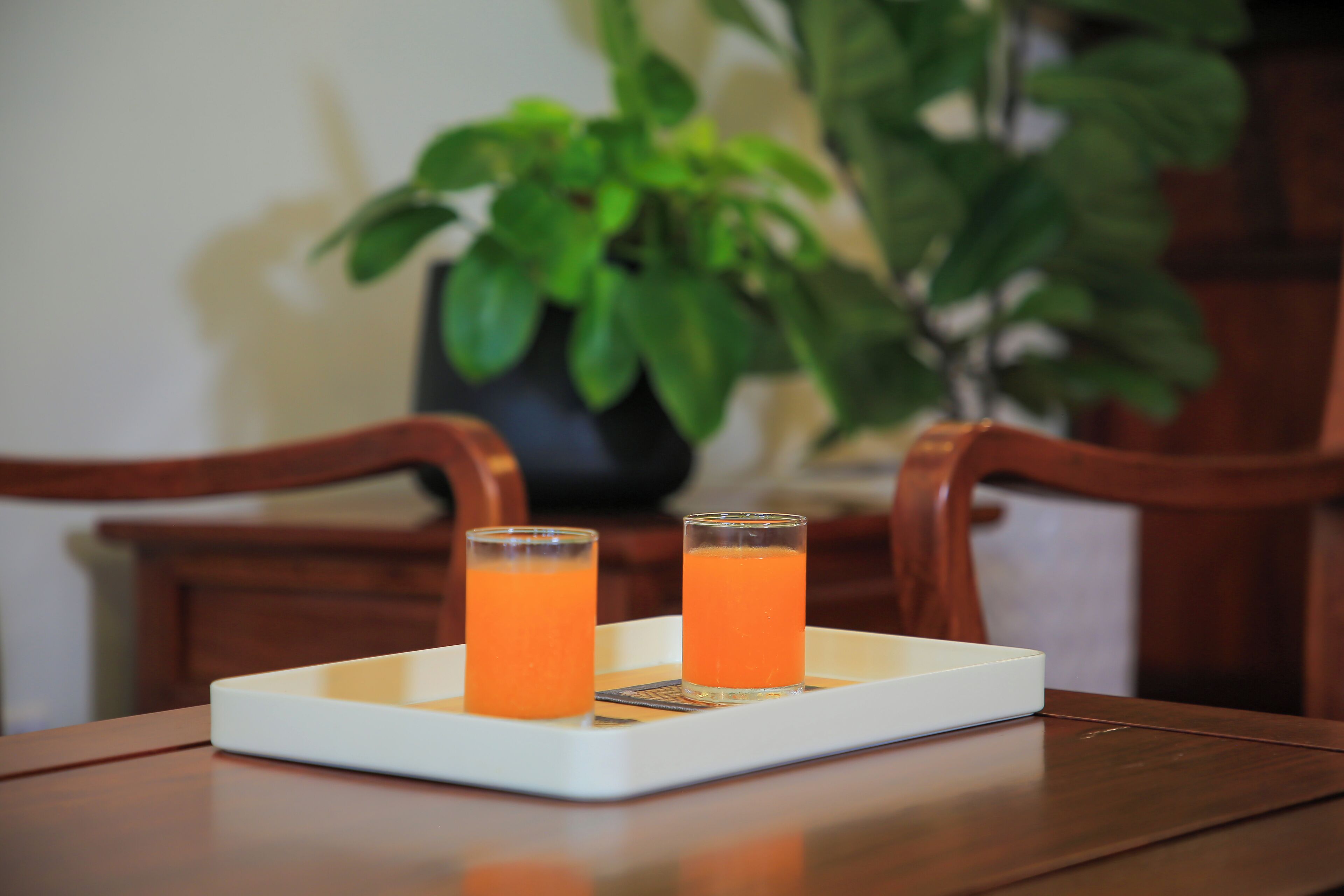 Dos vasos de jugo de naranja sobre una bandeja blanca en una mesa de madera.