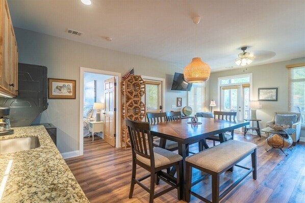 A spacious kitchen with granite countertops, a dining area with a wooden table and chairs, and a cozy seating area with a sofa and armchair. - Alpine Village Condo A | Location, Location, Location, Across From RIver and Tubing (Helen)