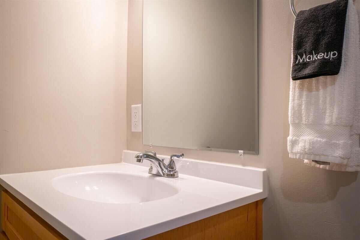 Une salle de bain avec un lavabo blanc, un miroir et un porte-serviettes sur lequel est posée une serviette noire étiquetée « Maquillage ».