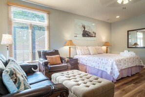 A bedroom with a bed, a chair, a sofa, a nightstand, and a lamp.