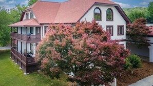 Une maison à deux étages, avec un toit rouge et des murs blancs, dotée d’un balcon au rez-de-chaussée.