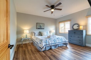 A bedroom with a bed, a ceiling fan, a dresser, a nightstand, and a wall-mounted lamp.