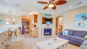 A spacious living area with a fireplace, a dining table with chairs, a sofa, and a ceiling fan. - Dover Vistas - Ocean View w/ Rooftop Terrace, Firepit, Fast WiFi, AC & Parking! (San Diego)