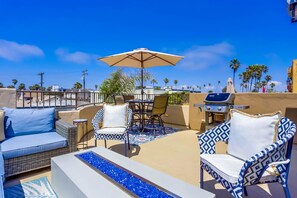 A rooftop patio with outdoor furniture, a grill, and a view of palm trees. - Dover Vistas - Ocean View w/ Rooftop Terrace, Firepit, Fast WiFi, AC & Parking! (San Diego)