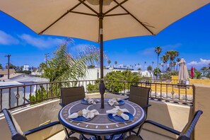 A round table with four chairs and a central umbrella on a balcony overlooking a cityscape with palm trees and buildings. - Dover Vistas - Ocean View w/ Rooftop Terrace, Firepit, Fast WiFi, AC & Parking! (San Diego)