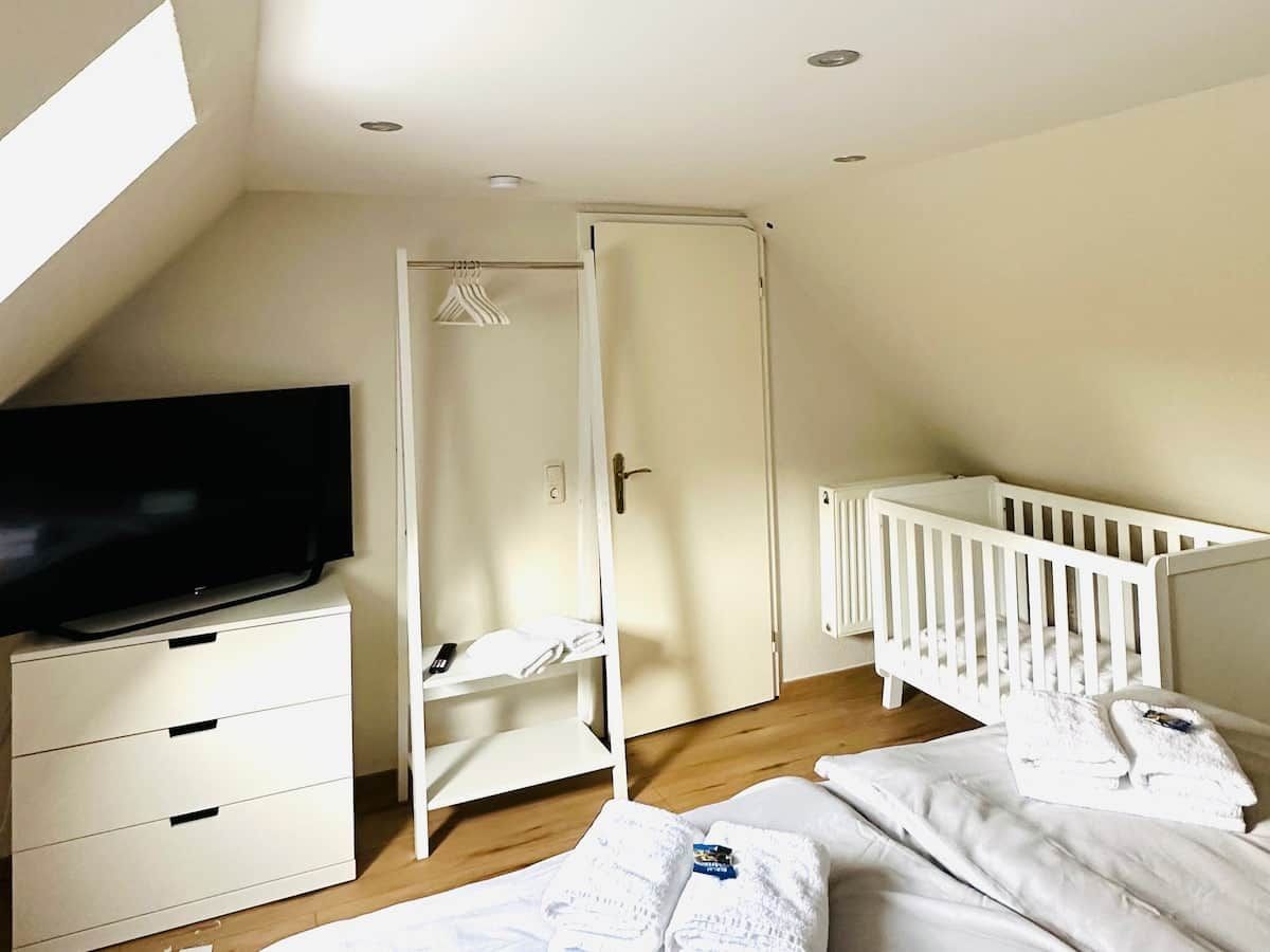 Ein Zimmer mit Fernseher auf einer Kommode, einem Babybett und einem Kleiderschrank.