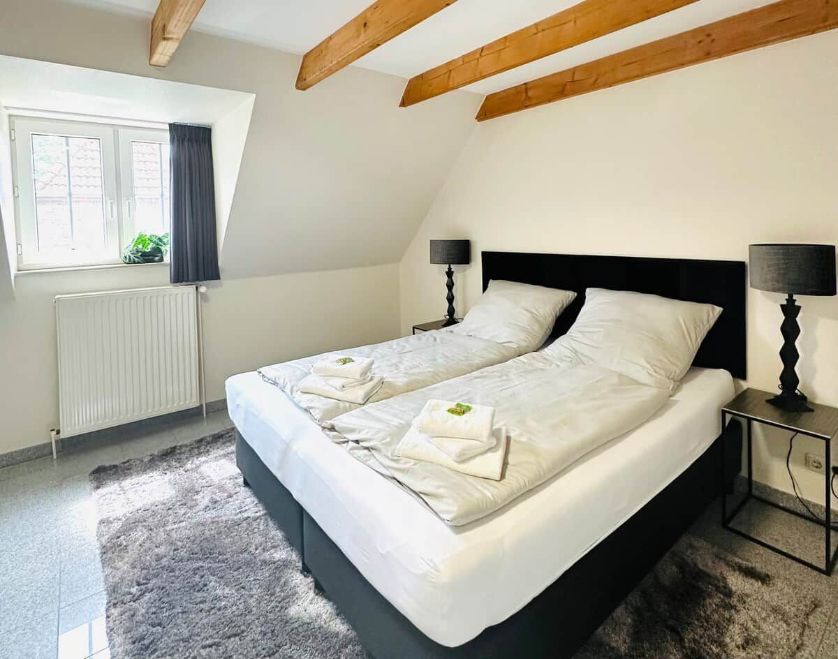 Une chambre avec un grand lit, deux tables de chevet, une fenêtre avec des rideaux et un radiateur.