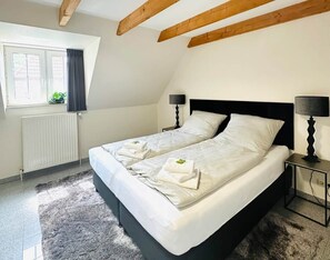 A bedroom with a large bed, two bedside tables, a window with curtains, and a radiator.