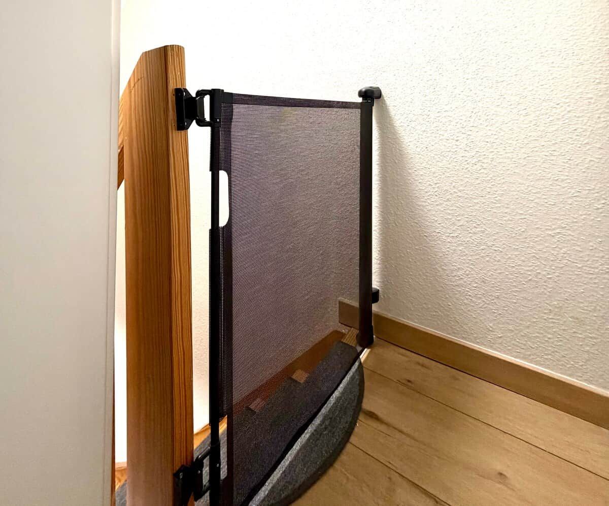 A corner of a room with a wooden floor, a white textured wall, and a black metal object that appears to be a gate or barrier.