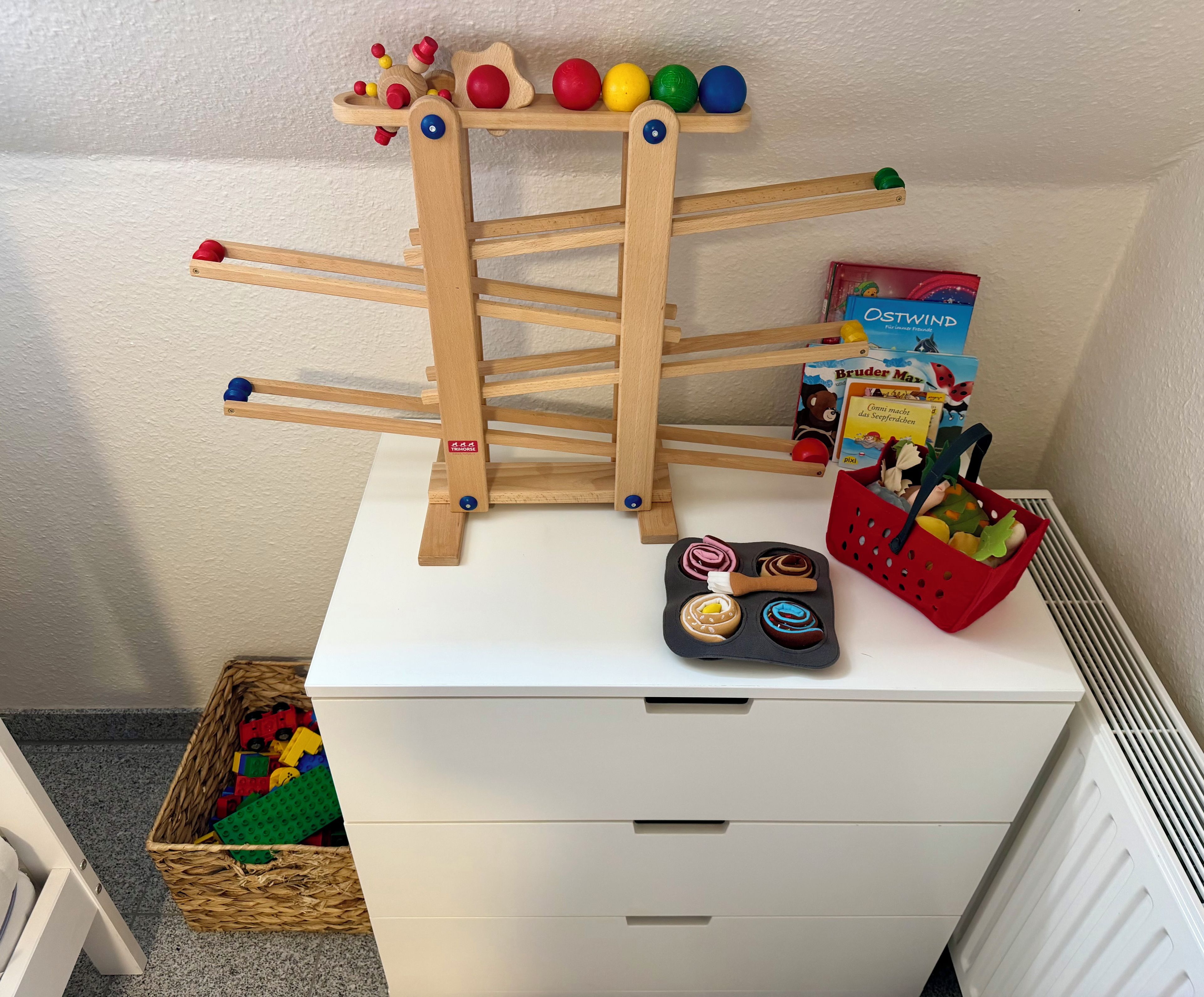 Ein weißer Stauraum mit einer hölzernen Spielleiter, bunten Bällen und Kinderbüchern.
