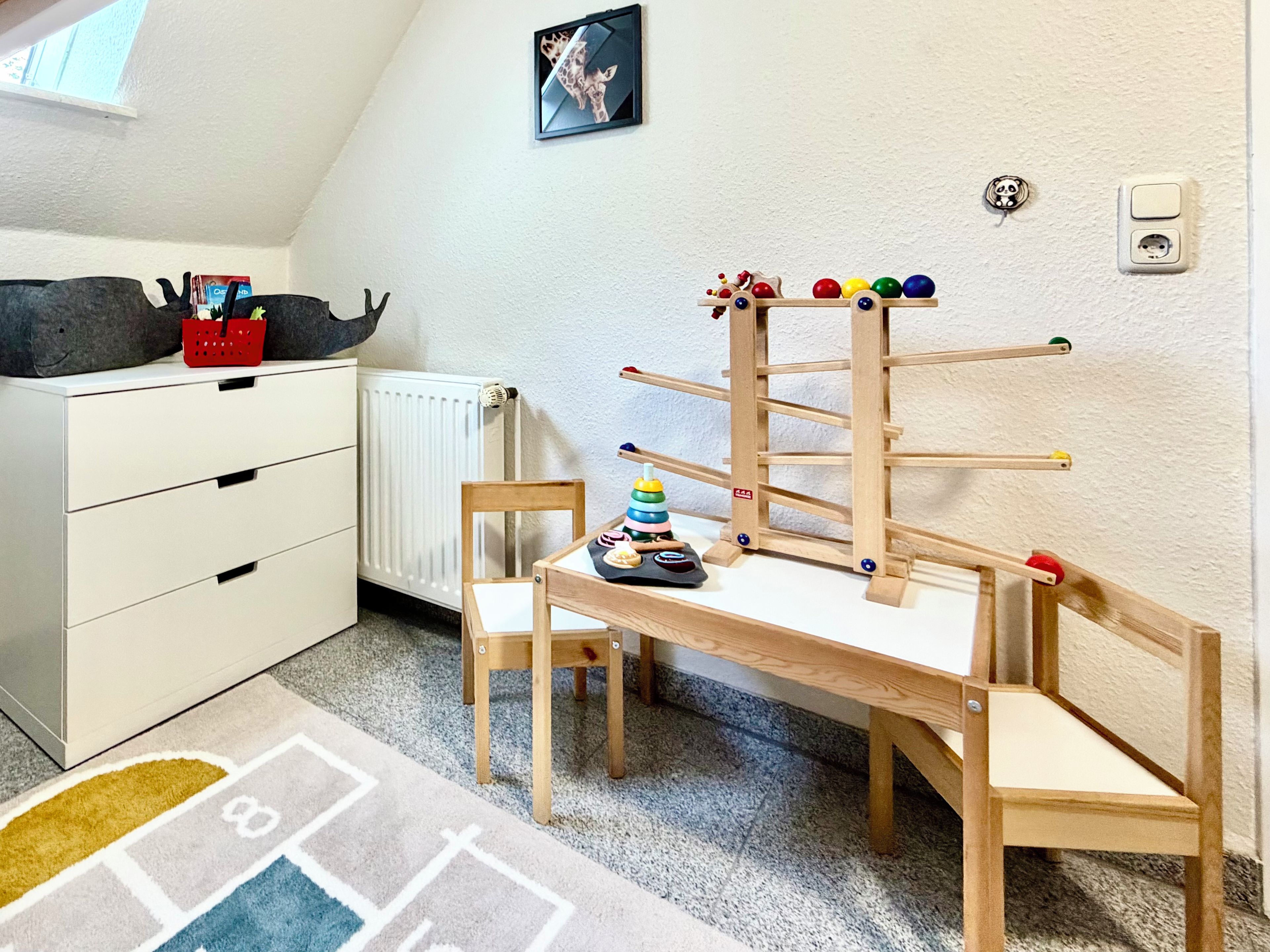 A child's play area with a wooden table, chairs, a hanging ball rack, and a radiator.