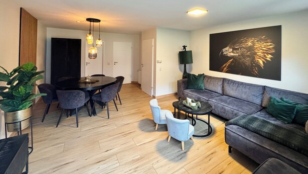 Ett modernt vardagsrum med en grå soffa, ett runt matbord med stolar, ett soffbord och en stor tavla med en örn på väggen.