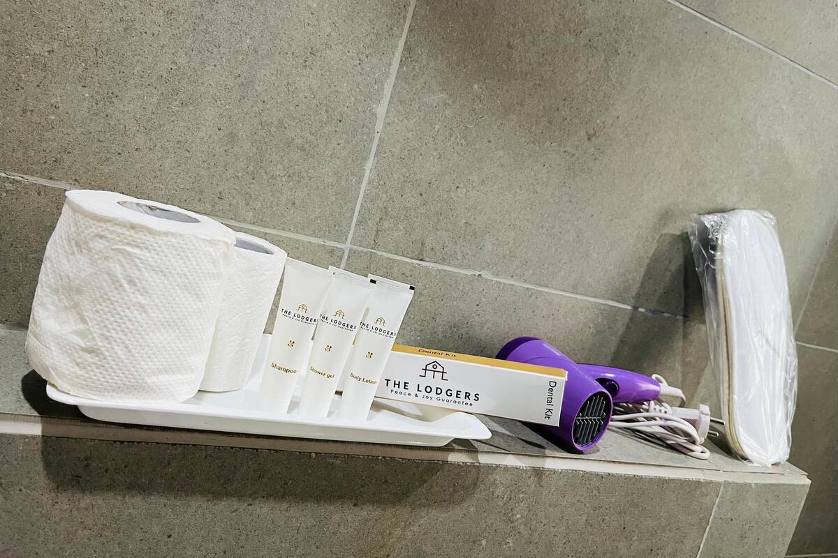 Un estante de baño con artículos de aseo, incluyendo un paquete de papel higiénico, un cepillo de dientes, un rastrillo de afeitar y un secador de pelo morado.