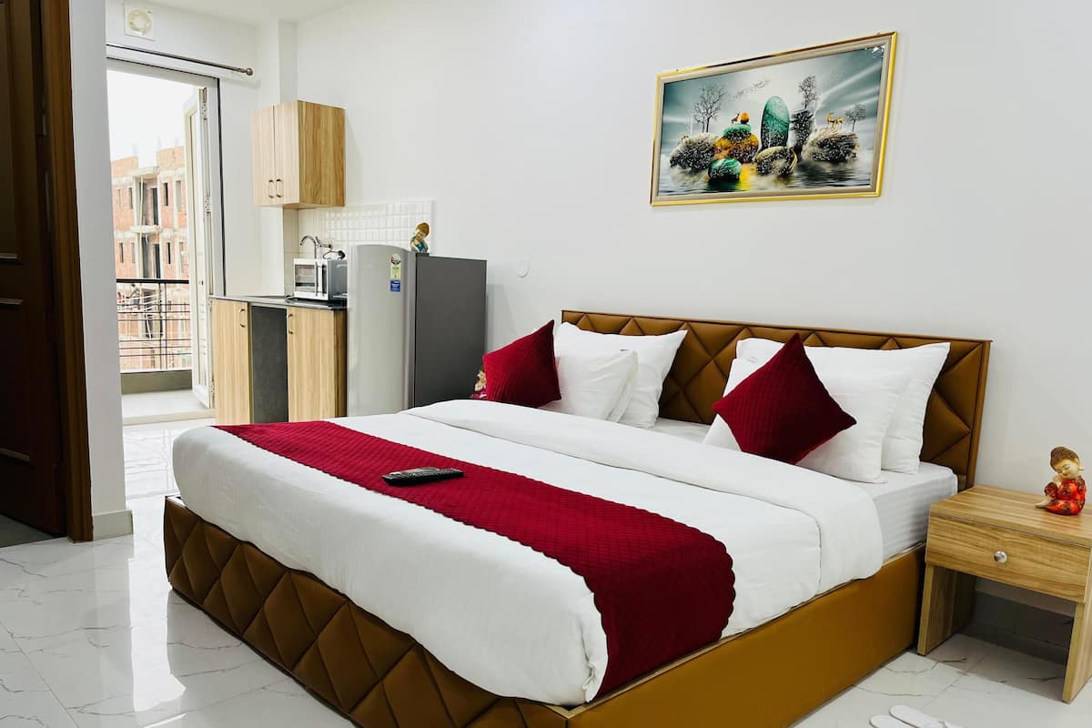 Una cama bien tendida con una manta y almohadas rojas, una mesita de noche con una figurita, y un cuadro en la pared.