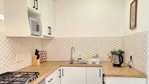 Een kleine keuken met witte kastjes, een magnetron, een gasfornuis en een spoelbak.