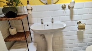 Een badkamer met een wit wastafelmeubel, toilet en een plank met handdoeken en toiletartikelen.