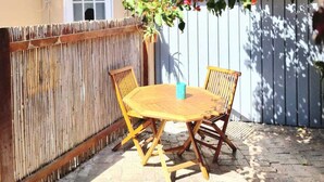 Een terras met een houten tafel en stoelen, een bamboe hek en een bloeiende plant.
