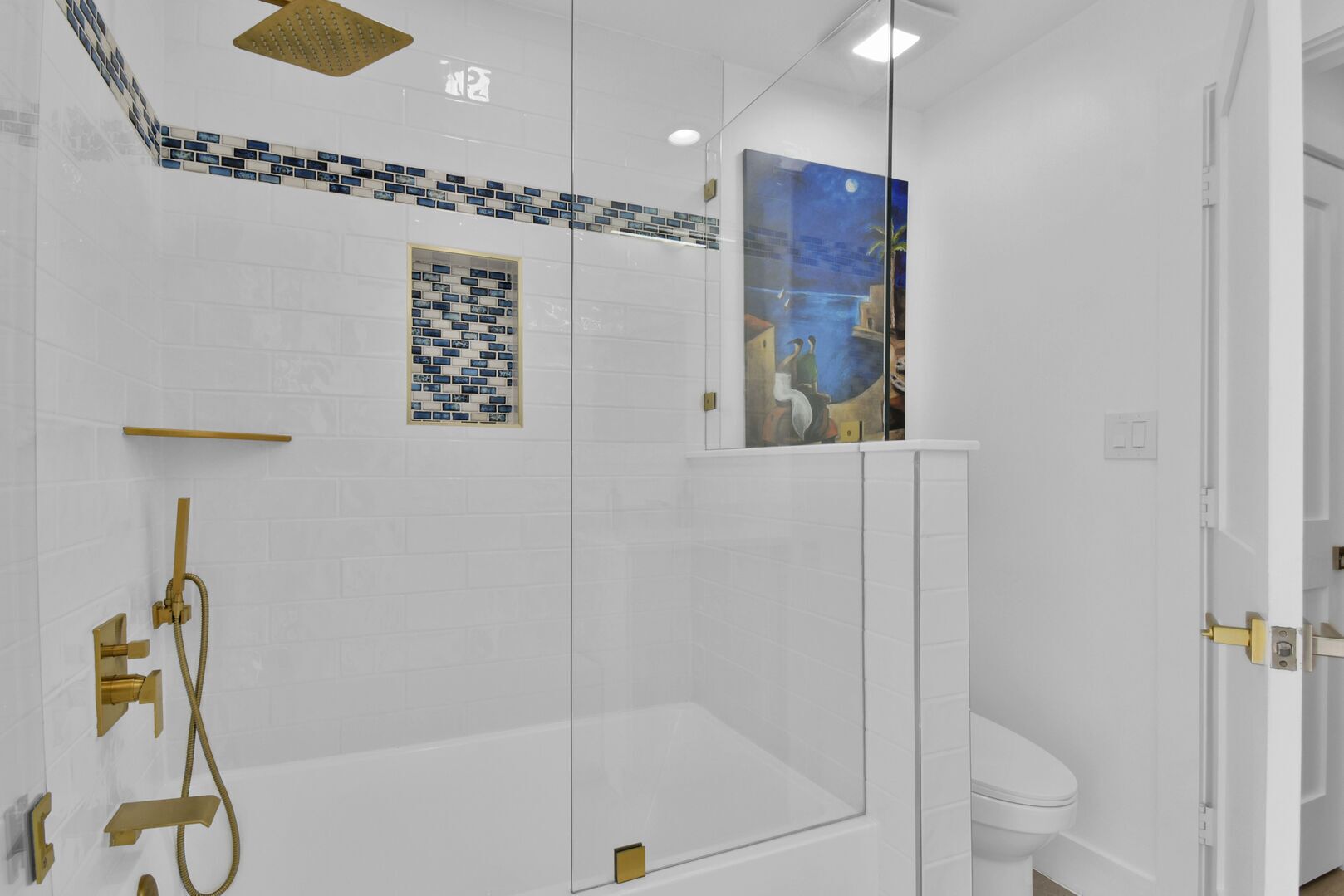 Un baño moderno con ducha de vidrio, paredes de azulejos blancos y un cuadro que representa una escena nocturna.