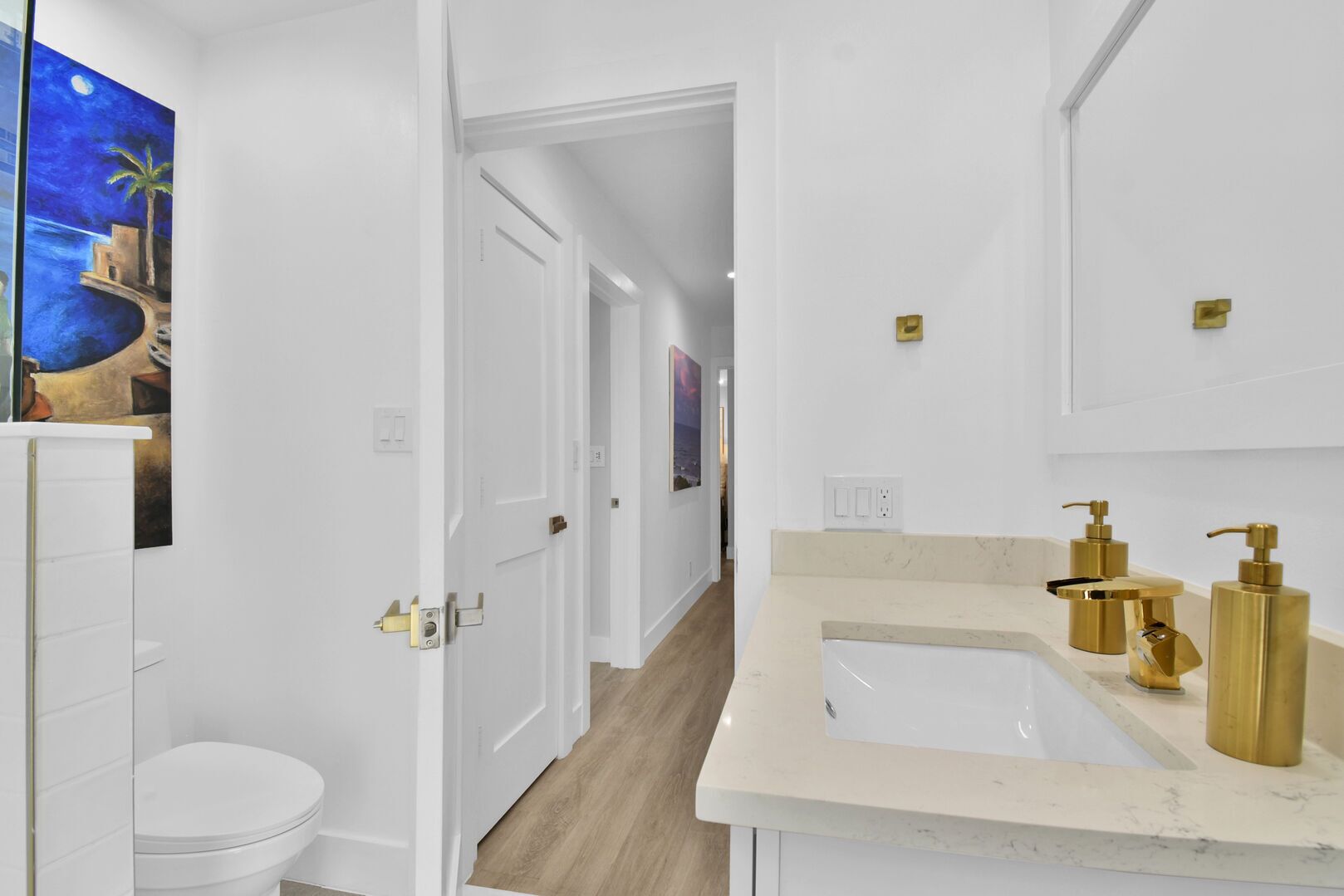 Une salle de bain moderne avec des toilettes blanches, un comptoir beige et des accessoires dorés.