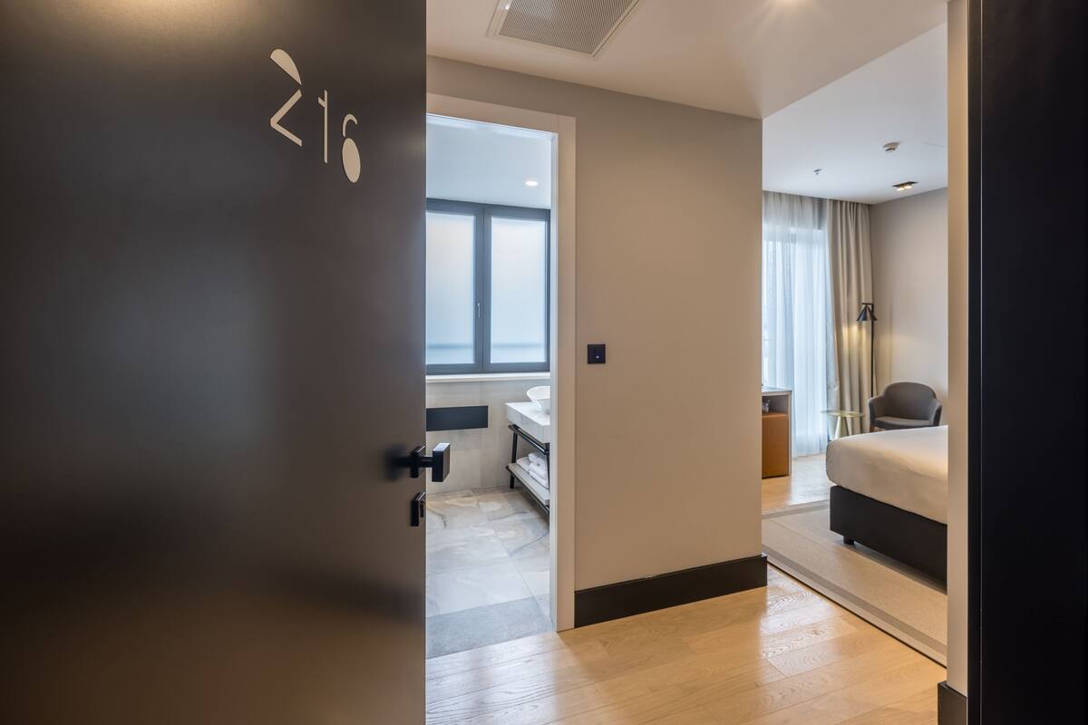 A modern hotel room with a bed, a desk, and a window.