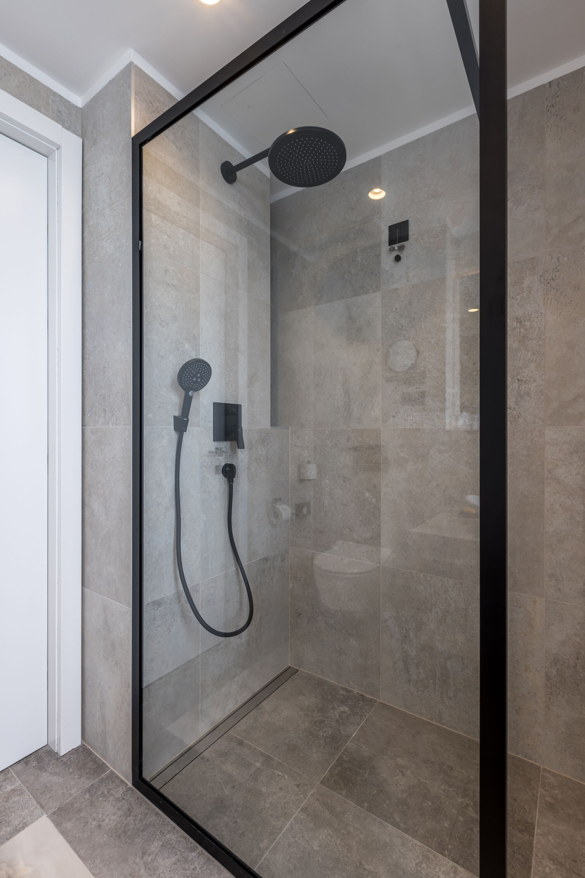 A modern shower with a glass enclosure, a handheld showerhead, and a wall-mounted control panel.