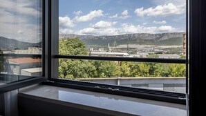 A view from a window overlooking a cityscape with mountains, industrial buildings, and greenery.