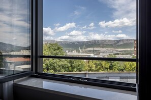 A view from a window overlooking a cityscape with mountains, industrial buildings, and greenery.