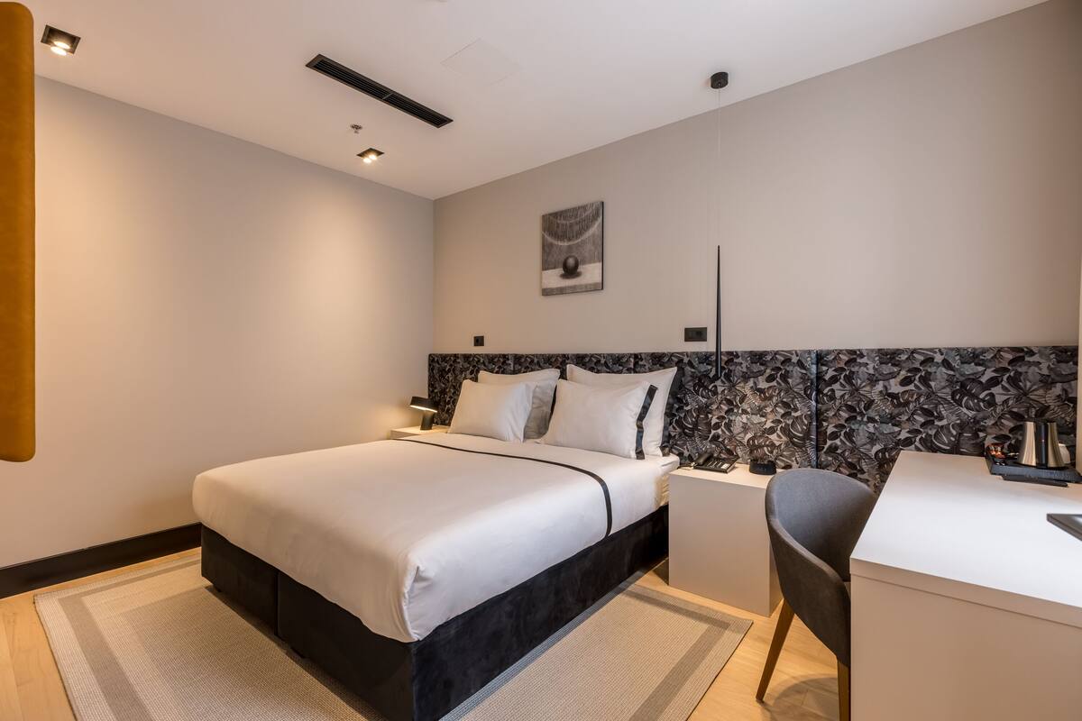 A modern hotel room with a large bed, a desk, and a chair.
