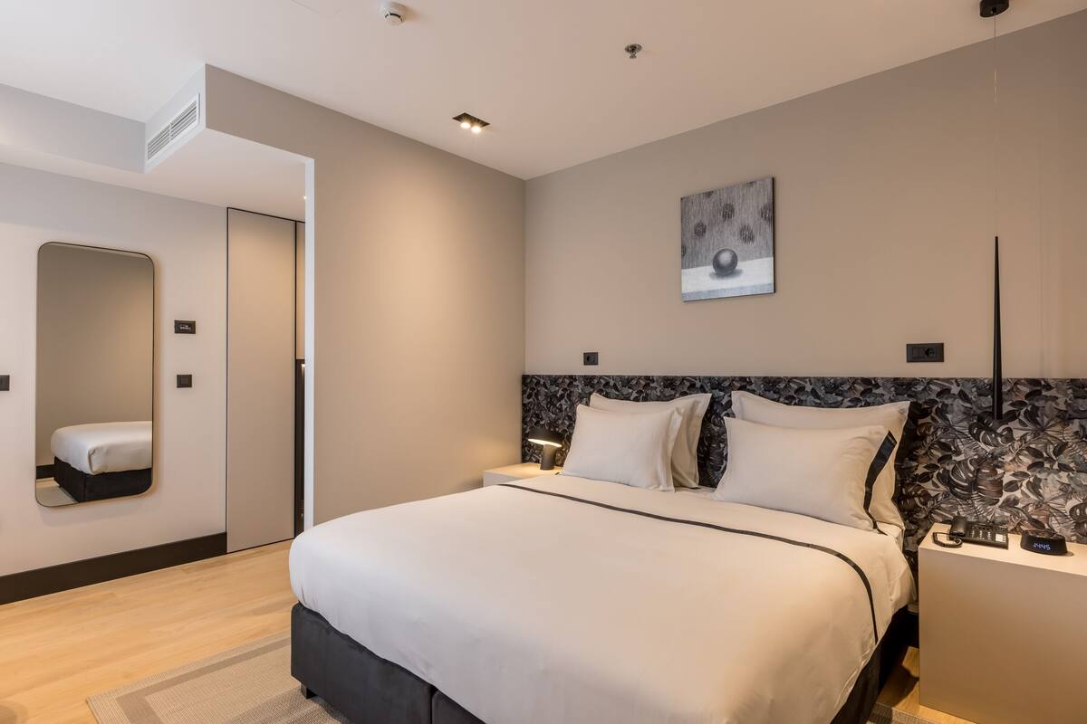 A modern hotel room with a large bed, bedside tables, a mirror, and a wall-mounted artwork.