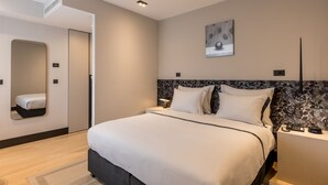 A modern hotel room with a large bed, bedside tables, a mirror, and a wall-mounted artwork.