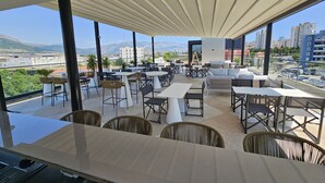 A rooftop terrace with outdoor seating, a view of the cityscape, and mountains in the distance. - Cora Hotel (Split)