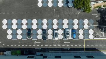 Vista aérea de un estacionamiento con varias filas de espacios, una parada de taxis y un edificio con múltiples ventanas en primer plano.