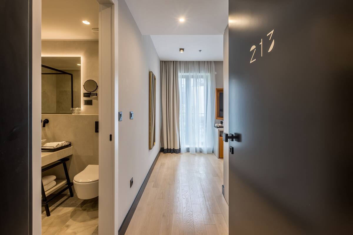 A modern hotel room with a wooden floor, a large mirror, a toilet, and a sink.