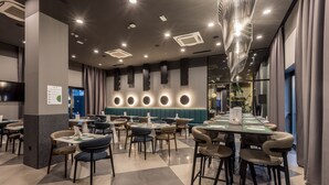 A modern restaurant with a checkered floor, round tables, and a row of circular light fixtures on the wall. - Cora Hotel (Split)