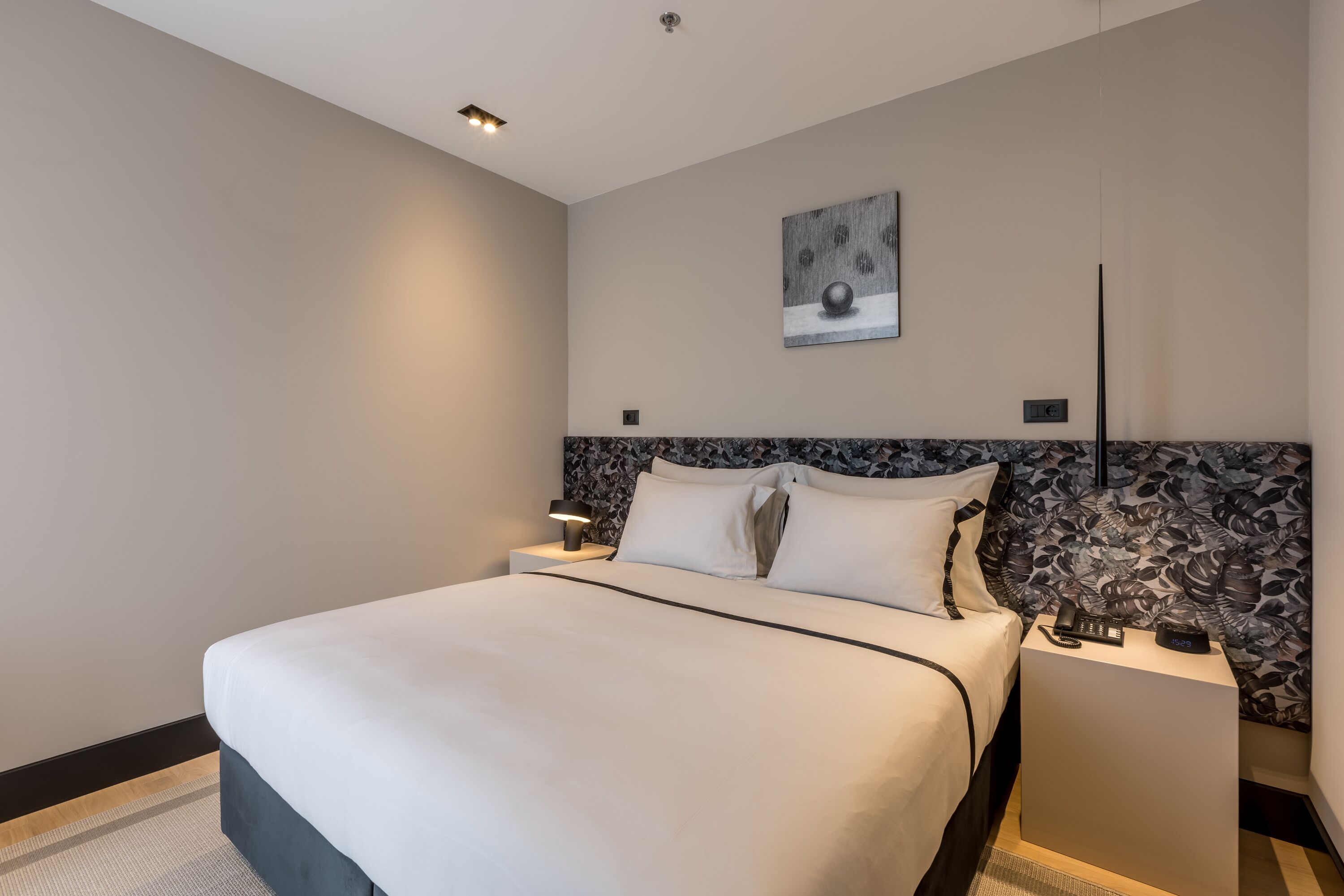 Una habitación de hotel moderna con una cama grande, una mesita de noche con lámpara y una obra de arte colgada en la pared.