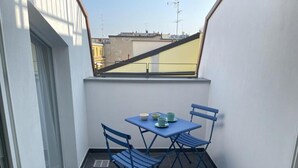 Un balcón pequeño con una mesa y sillas, una ventana y vistas a edificios.