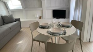 Un comedor con una mesa redonda dispuesta para cuatro personas, un sofá gris y un televisor montado en la pared.