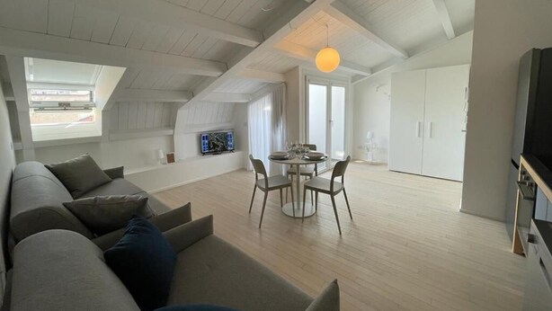 Amplio apartamento tipo loft con techos altos, zona de comedor y televisor en la sala.
