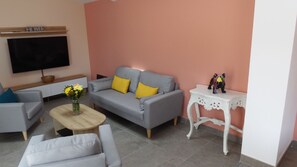 A living room with a grey sofa, a wooden coffee table, a white side table, and a flat-screen TV mounted on the wall.