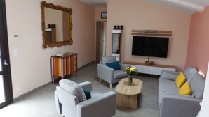 Una sala de estar con un sofá, sillones, una mesa de centro, un televisor y un espejo.
