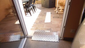 Un acceso a un patio exterior con un felpudo estampado, suelo de piedra y una mesa de comedor con sillas.