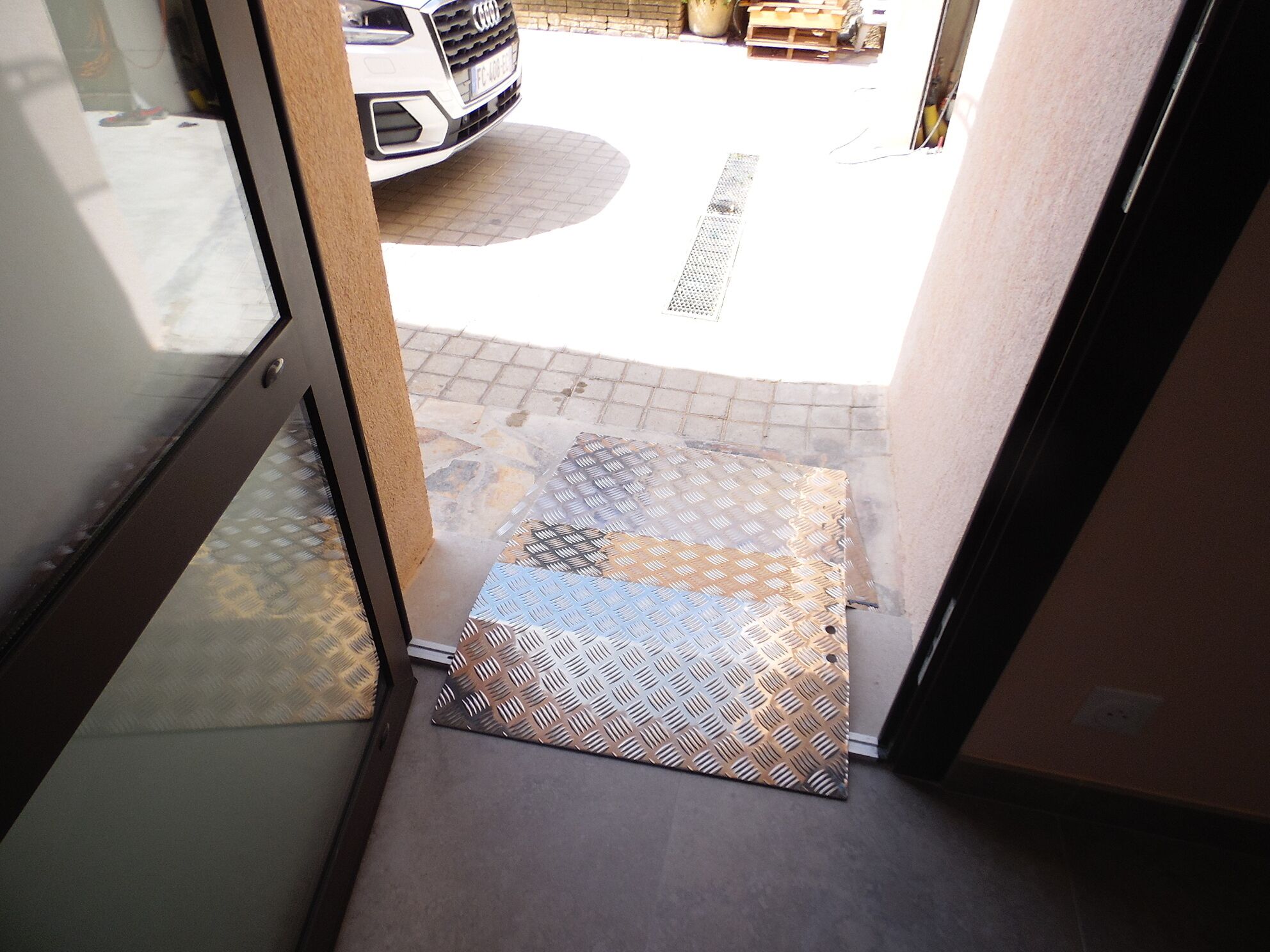 A doorway leading to a paved area with a patterned mat and a white vehicle parked outside.