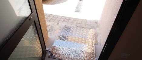A doorway leading to a paved area with a patterned mat and a white vehicle parked outside.