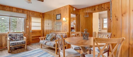 A wooden interior with a dining table, chairs, a sofa, and a ceiling fan.