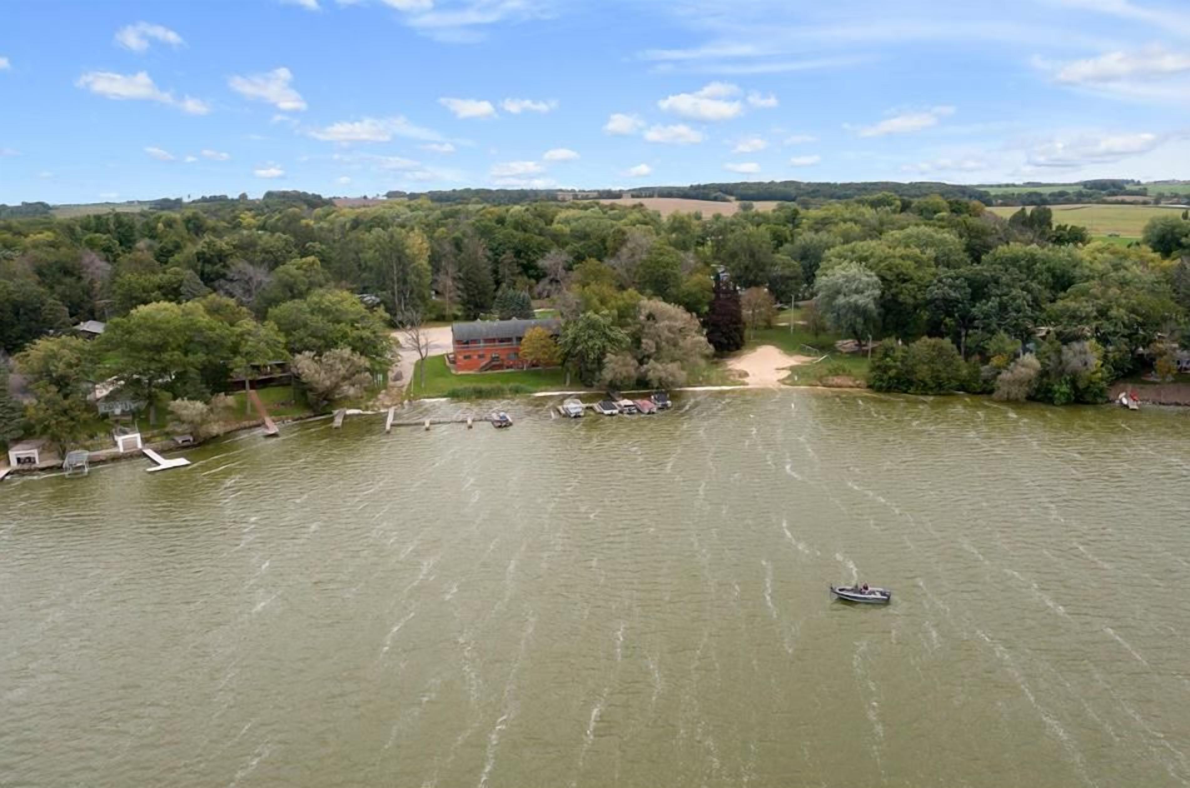 An aerial view of a riverside property with a dock, a boat, and a building surrounded by trees.