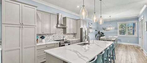 A modern kitchen with grey cabinets, a marble countertop, and a central island with bar stools.