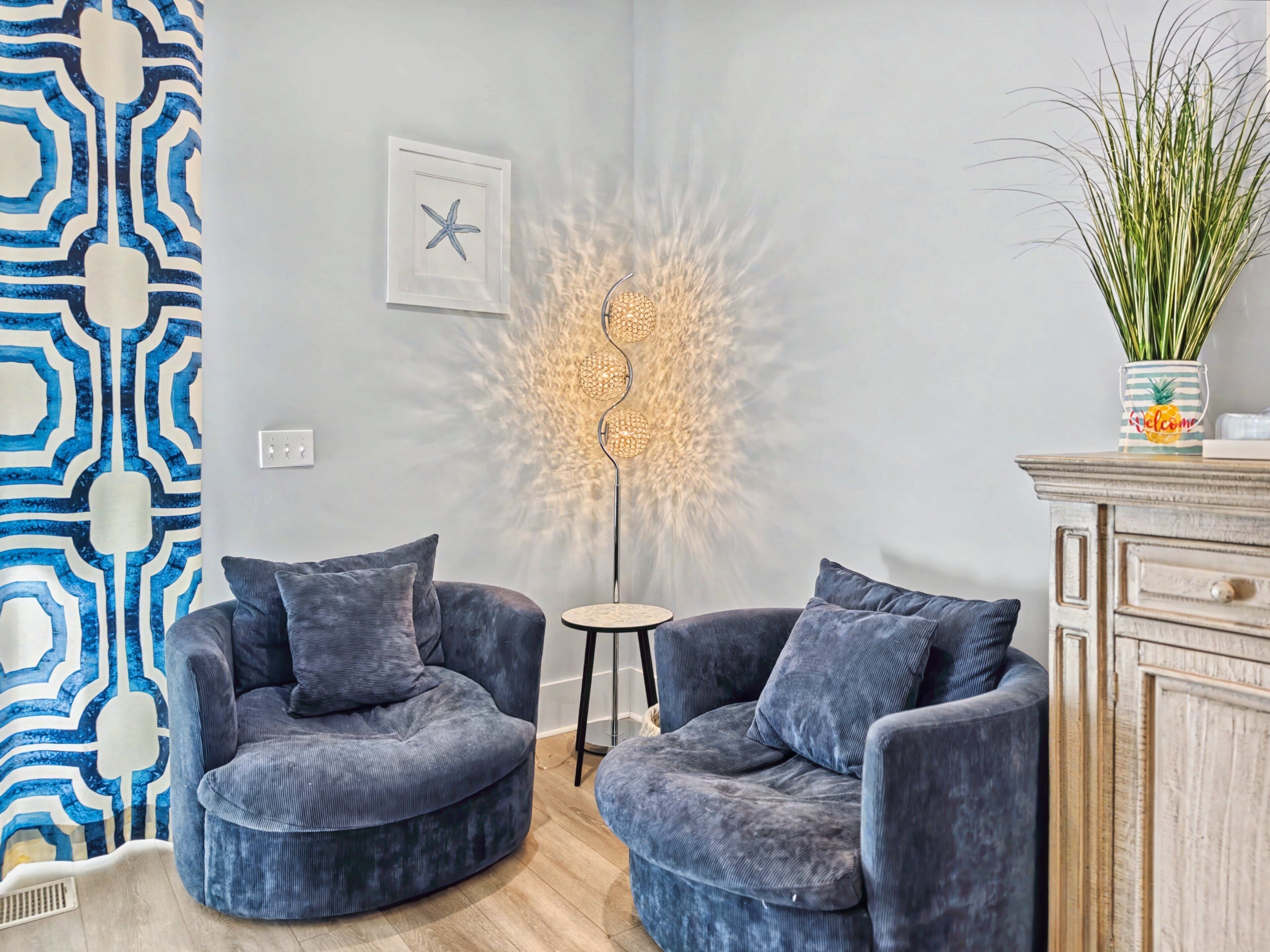 Un salón moderno con dos sillones grises, una mesita redonda, una lámpara decorativa y un cuadro de una estrella de mar colgada en la pared.
