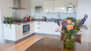 Una cocina moderna con armarios blancos, una campana extractora de acero inoxidable, un horno, un lavamanos y un florero con flores sobre la mesa.