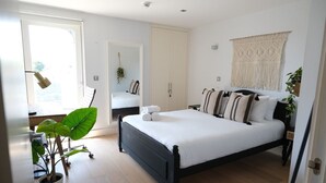 Un dormitorio con cama, una planta en maceta, un armario y un colgador de macramé en la pared.